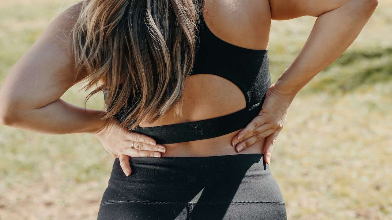woman holding lower back in pain outdoors illustrating pelvic floor dysfunction and lower back pain relation