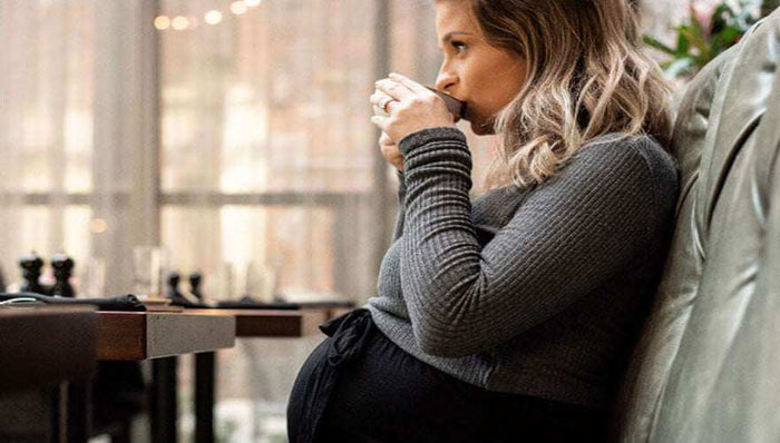 Pregnant woman drinking coffee and preparing for childbirth while sitting on a couch