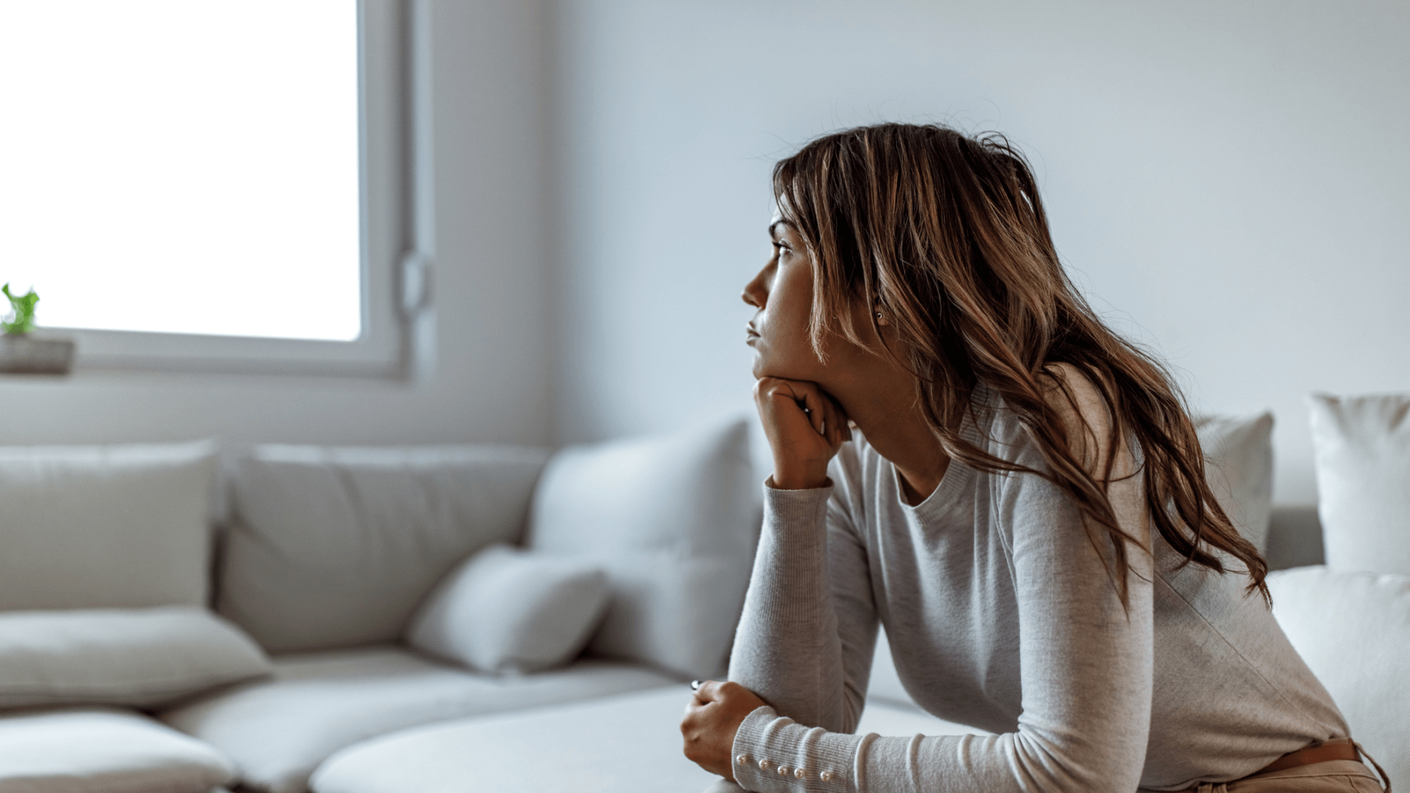 Woman sitting on couch indoors looking worried, representing urinary stress incontinence concerns.
