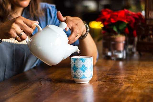 Woman pouring herbal tea into cup for natural overactive bladder remedy